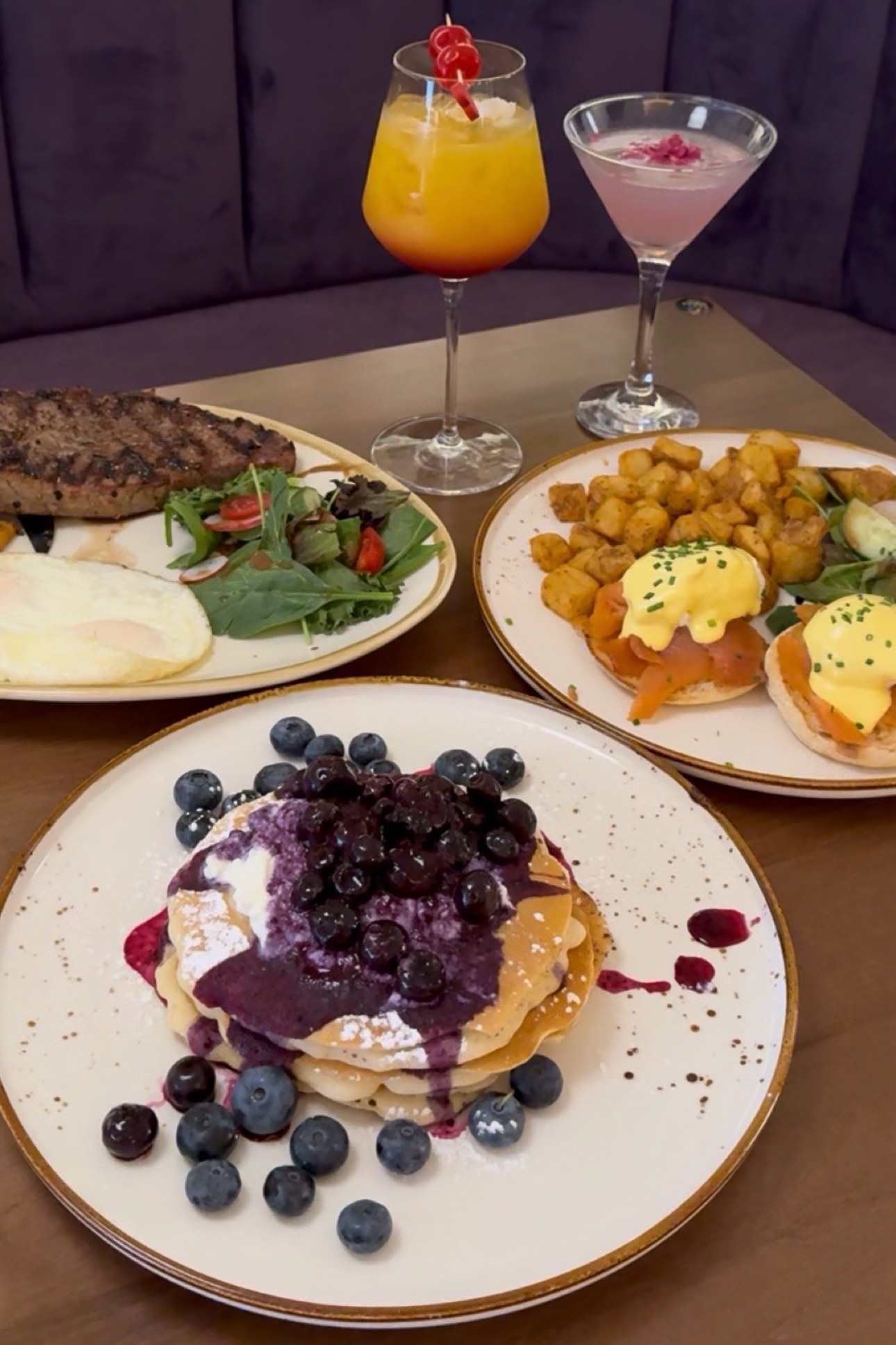 Sunlit brunch table with eggs benedict, a croissant, latte art and blush peonies in a chic café